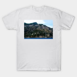 View in Amalfi coast at a huge mountain with rocky parts, greenery and buildings with a white boat underneath T-Shirt